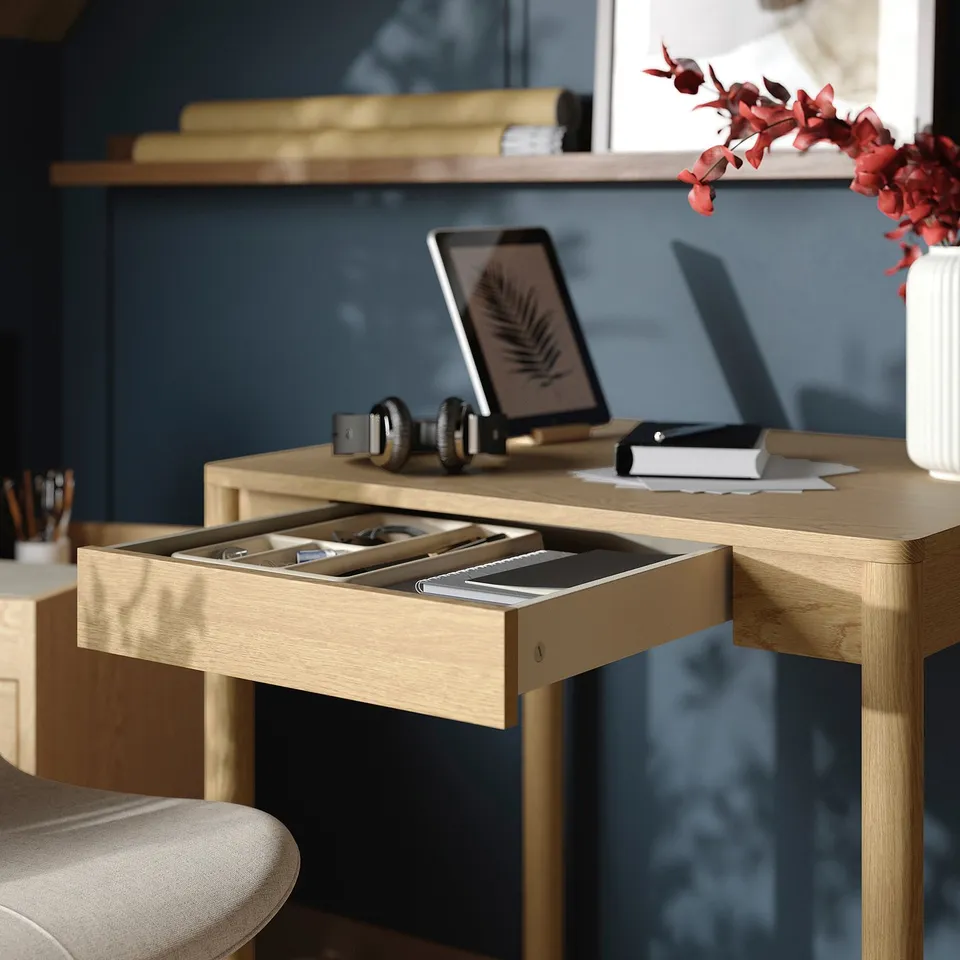 Desk with open drawer revealing organised items, including electronic devices and a book, showcasing its storage functionality.