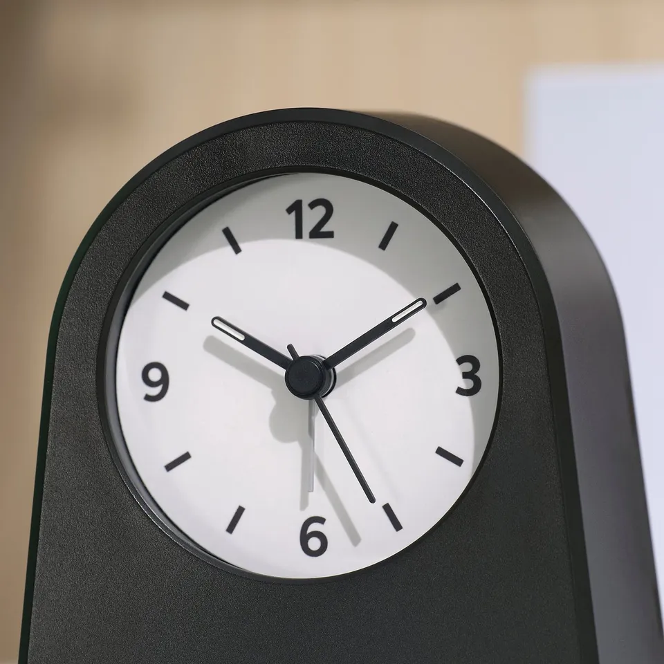 Black alarm clock with white face, black hands, and numbers at 3, 6, 9, and 12. Hands point at 9:25.