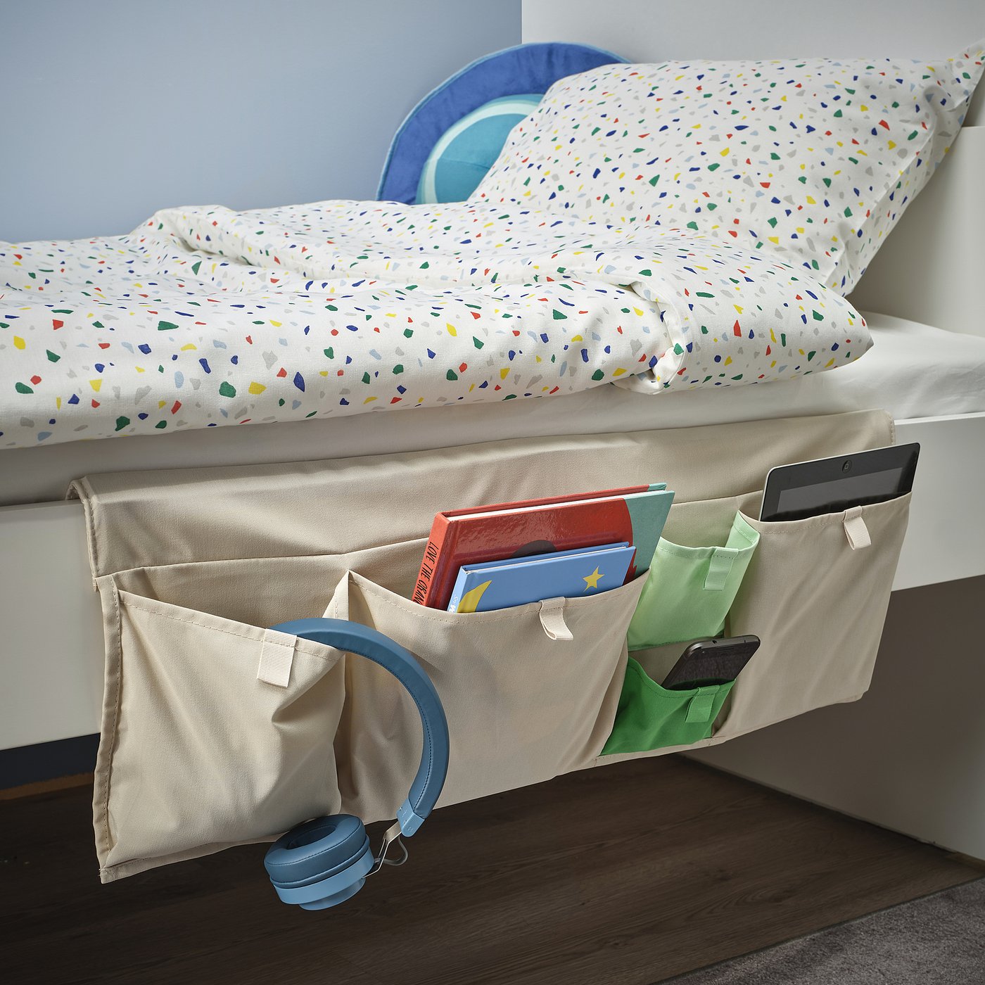 Bedside organiser hangs on bed rail, holding books, tablet, phone, and headphones. Helps keep items organised and close at hand.