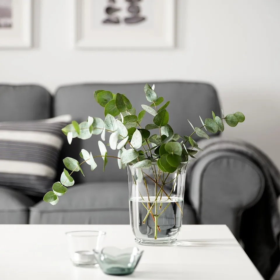 Small POMP glass vase, clear, with greenery on table near grey couch.