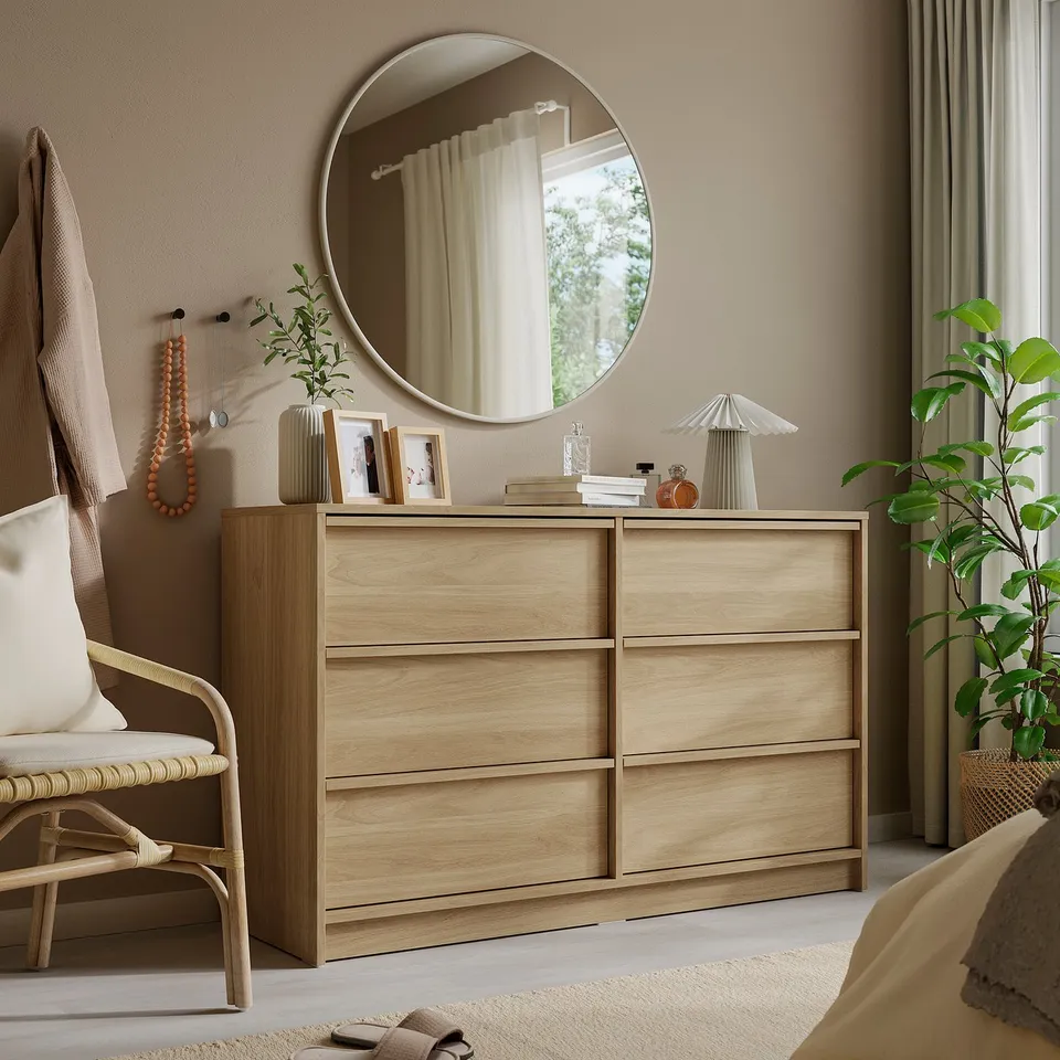 KVALMSÖ mirror in beige aluminium over light dresser, reflecting bright window and plant.