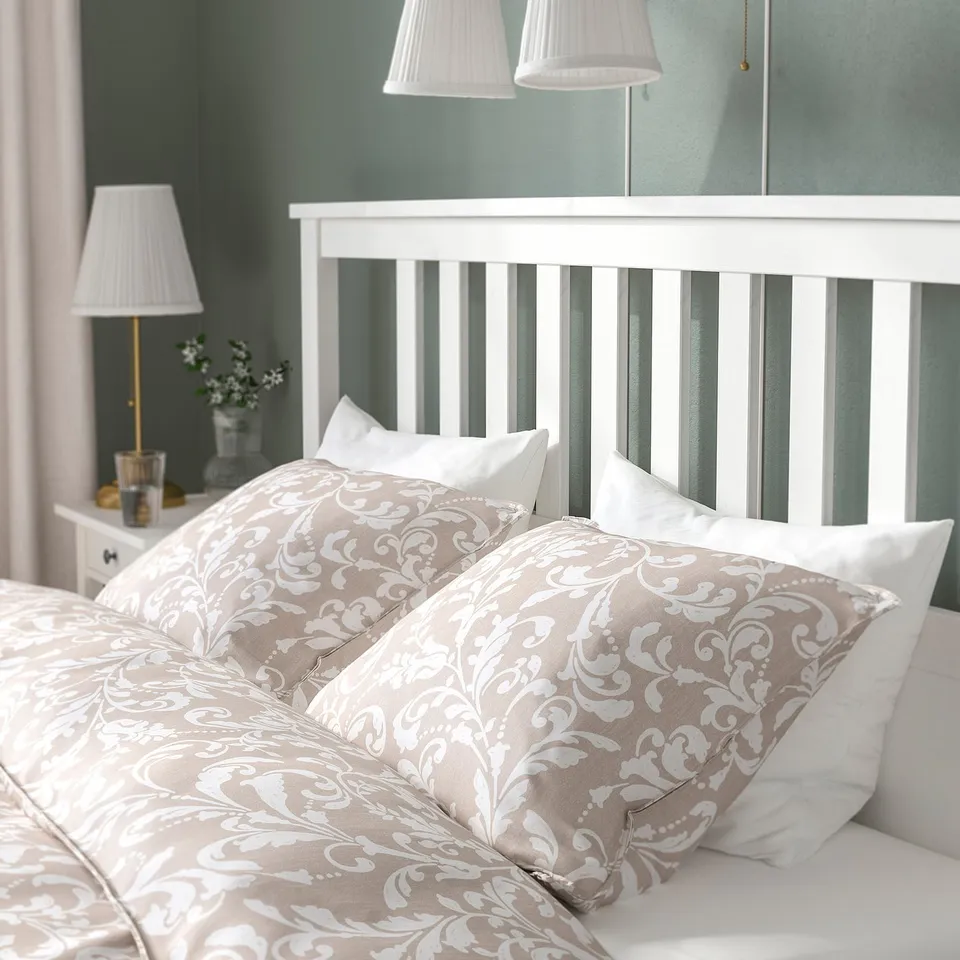 Bed with ornate pillows, two lamps, and floral decoration on bedside table.