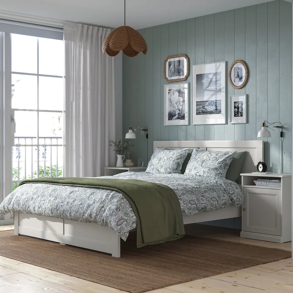 Modern bedroom with FÅGELFJÄLLET bed, tables, decor panelling, brass knobs, patterned bedding, green throw, and large window.