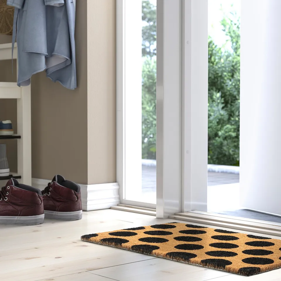 Black dotted TÅGFORDON doormat in entryway, near glass door.