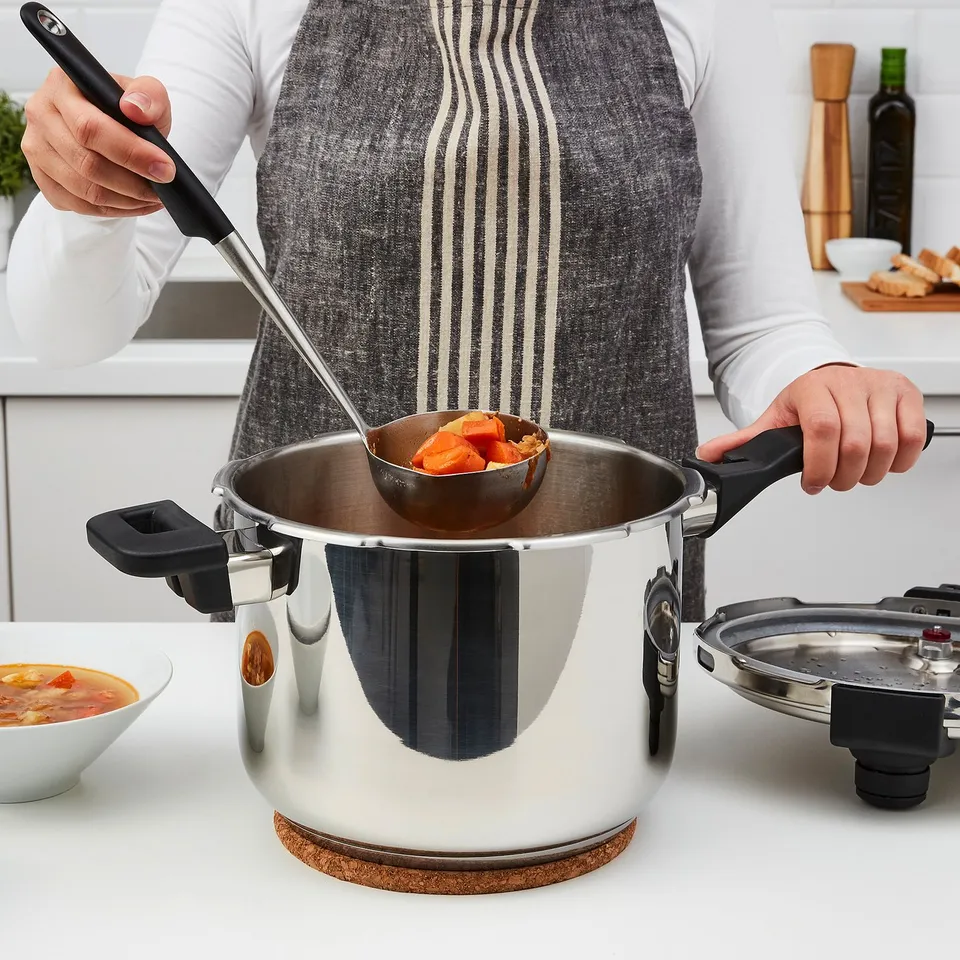 Person ladling orange soup from stainless steel pressure cooker with black handles.