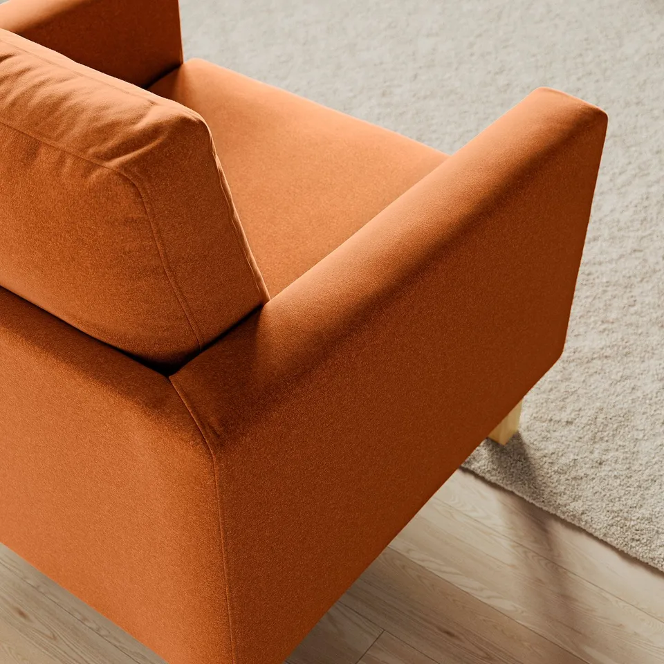 Close-up shot of an orange fabric armchair, highlighting its soft, supportive cushions and clean, modern design.