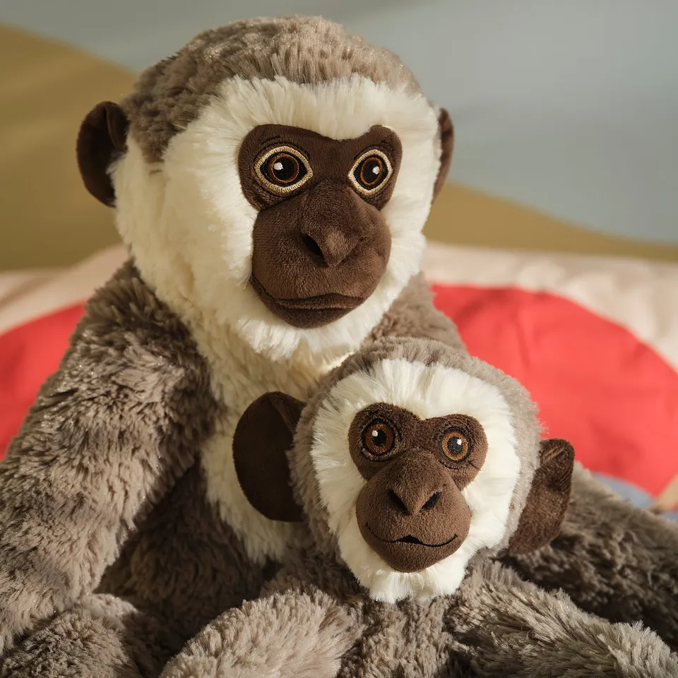 Two plush monkey toys, one larger and one smaller, made with soft, textured fur and detailed embroidered faces, posed closely together.