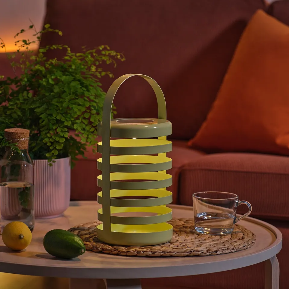 Modern lantern on table with fruits, cup, and plant.
