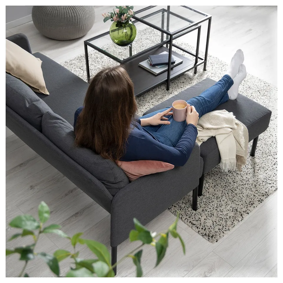Person on GLOSTAD sofa with coffee, cosy rug, and flowers.