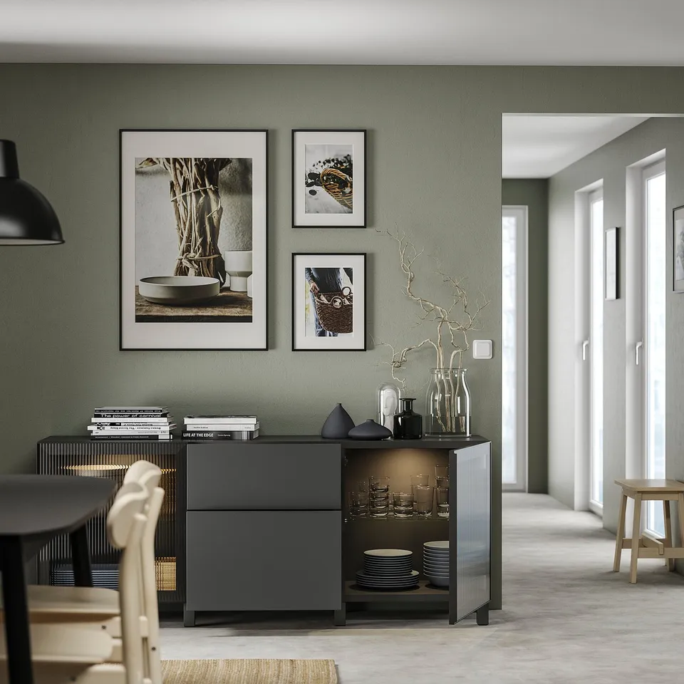 Modern living room with grey BESTÅ storage unit, white dishes, black vases, and framed wall art.
