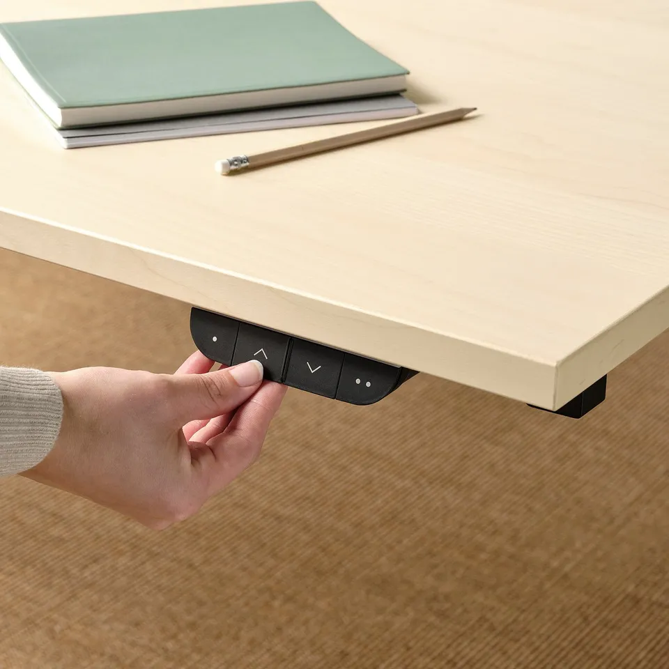 Hand presses button on desk controller. A sit/stand desk with memory settings and collision detection.