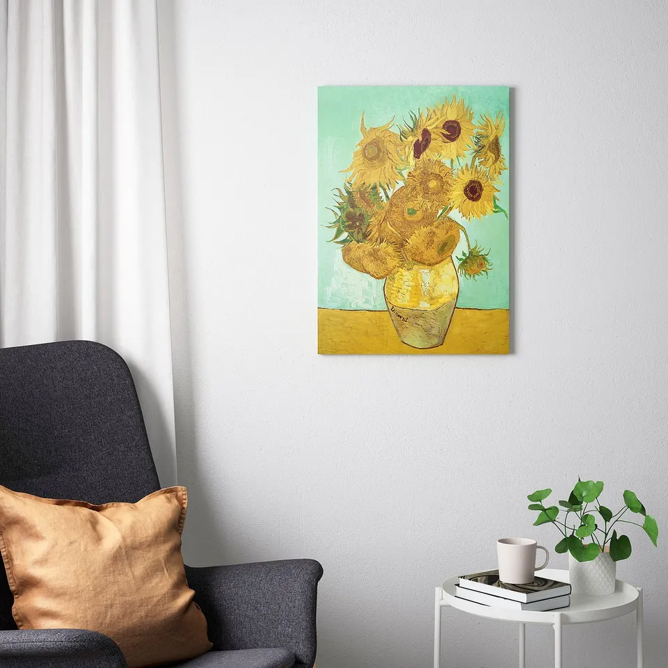 PJÄTTERYD van gogh sunflower print above couch with pillows, side table, books, cup, plant.