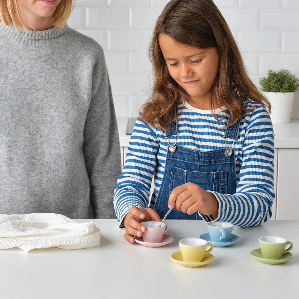 A young girl plays with a tea set, pouring tea into a cup.