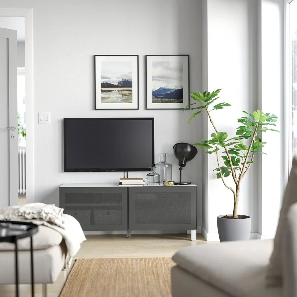 Modern living room with grey BESTÅ tv stand, flat screen tv, nature framed photos, white couch, round side table, and potted plant.