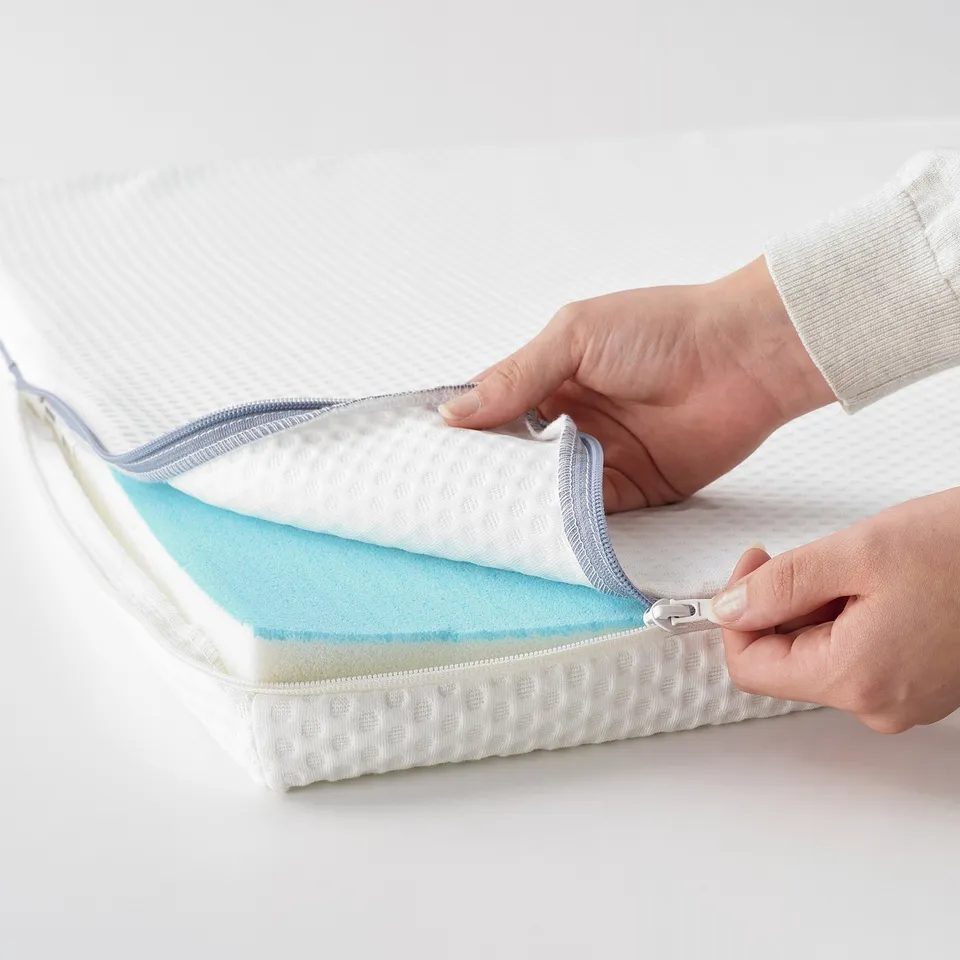 A person is unzipping a NÄSTABERG mattress topper, revealing its blue memory foam layer for pressure relief and temperature regulation.