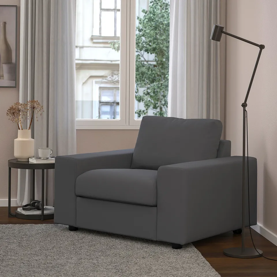 VIMLE grey armchair in modern living room by window. Accented with floor lamp and side table with vase and cup. Cosy and minimalist design.