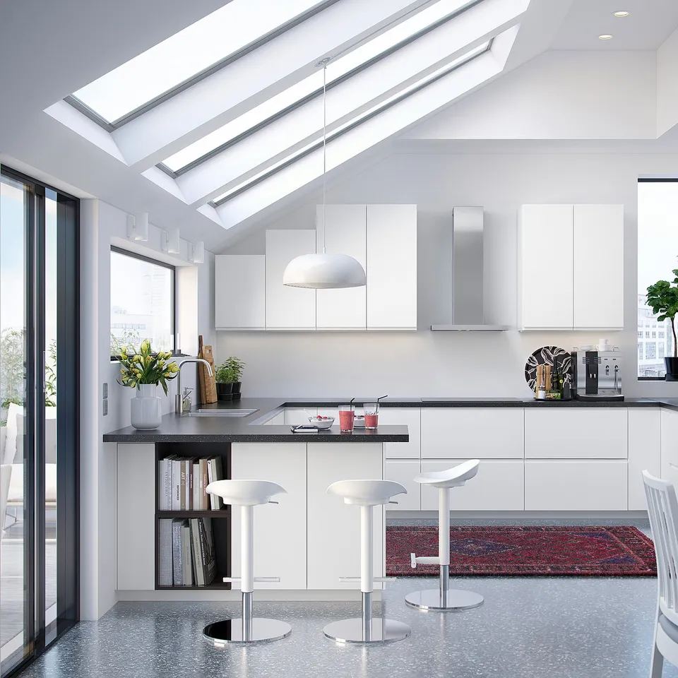 Modern white minimalist kitchen with white cabinets, dark countertops, and bar stools, featuring large windows and skylights.