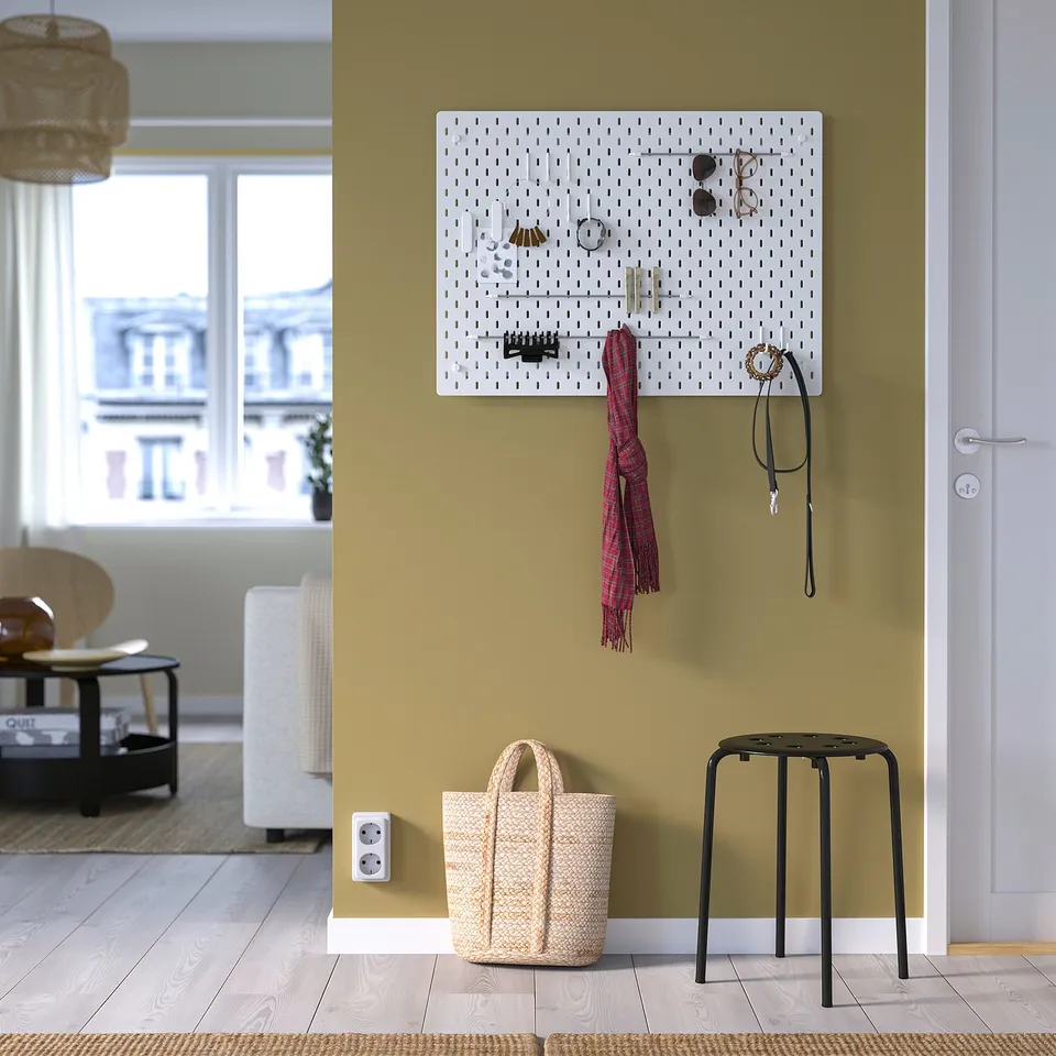 SKÅDIS pegboard with accessories on green wall; basket & stool below, window view.