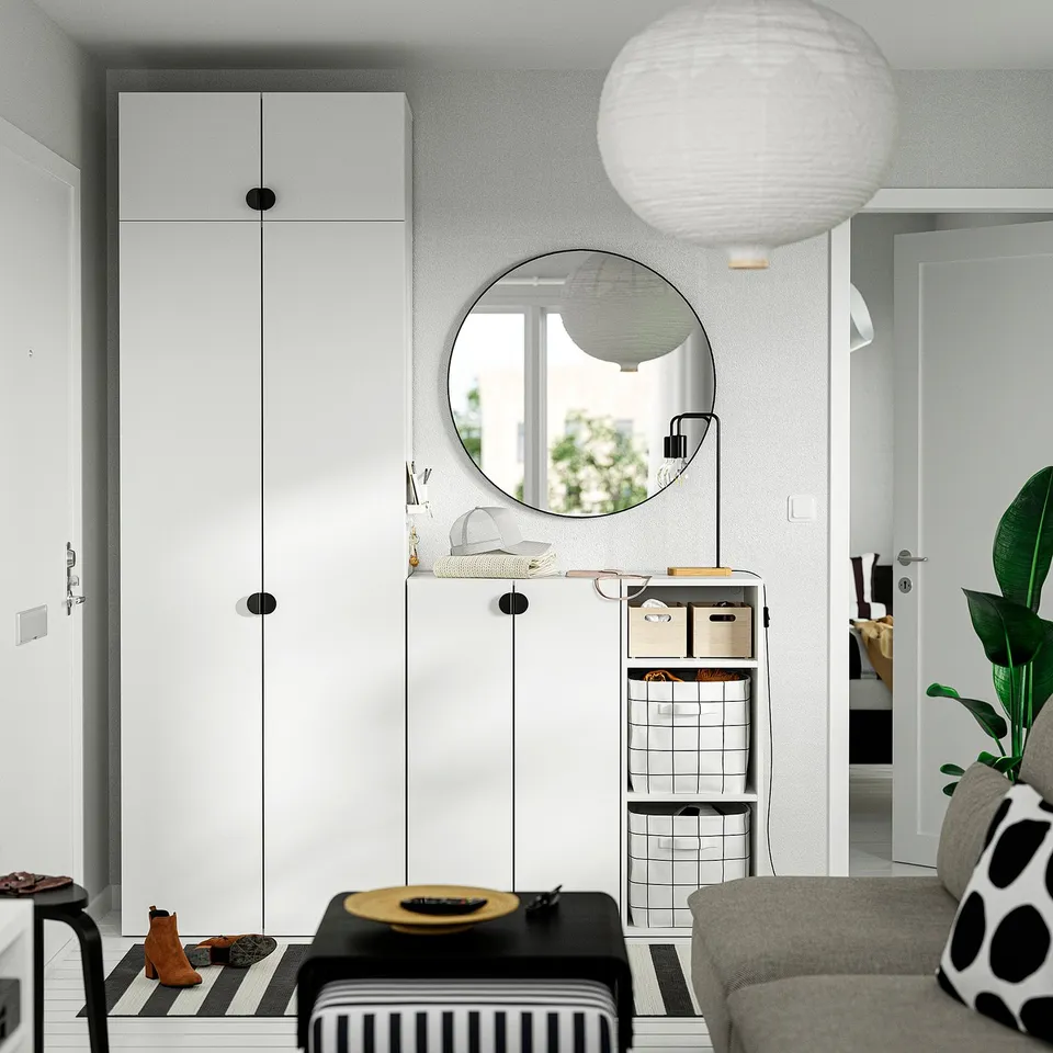 Modern living room with white storage units, a round mirror, striped bench, cosy sofa, and plant.
