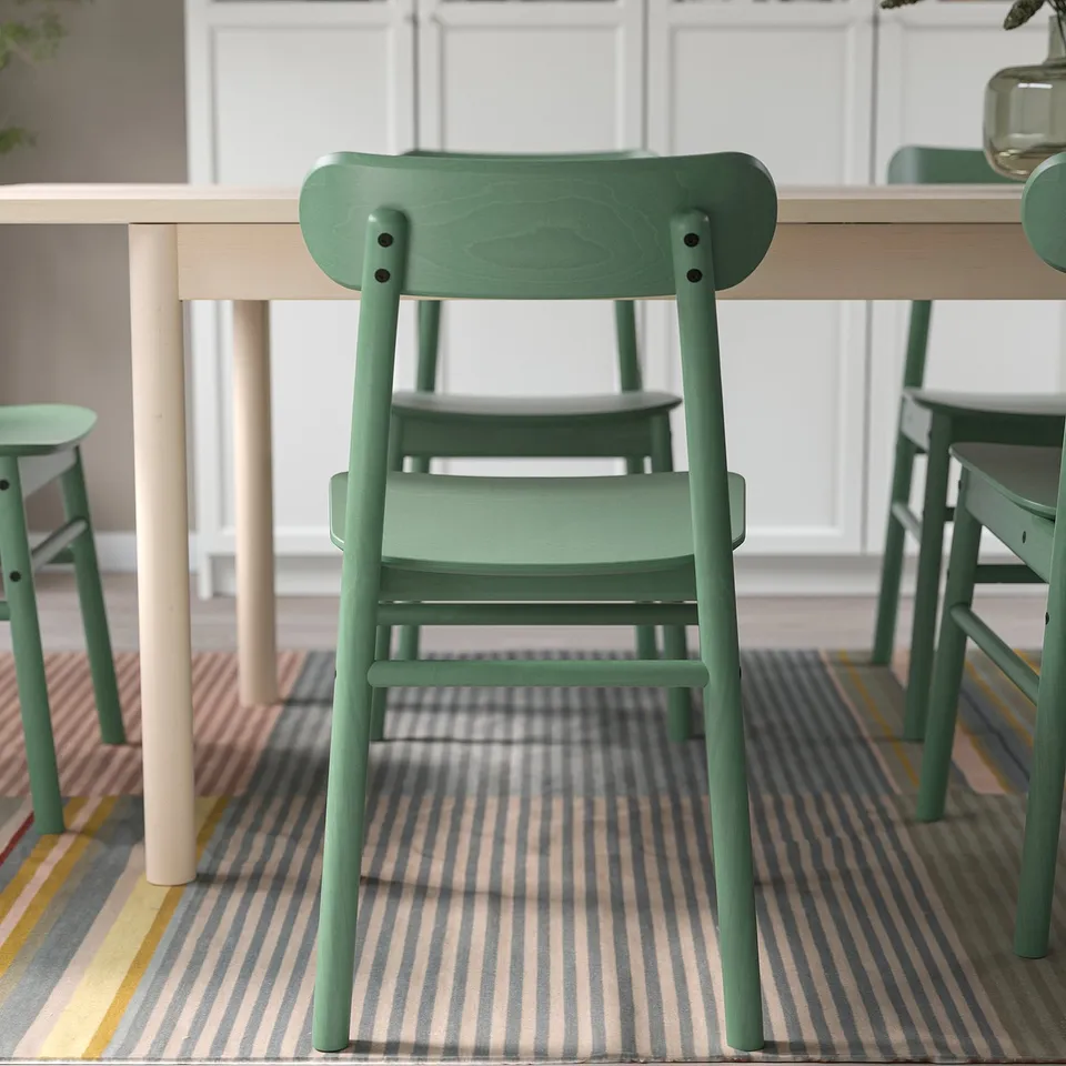 Green wooden chair at light wood table on striped rug - comfortable and robust.