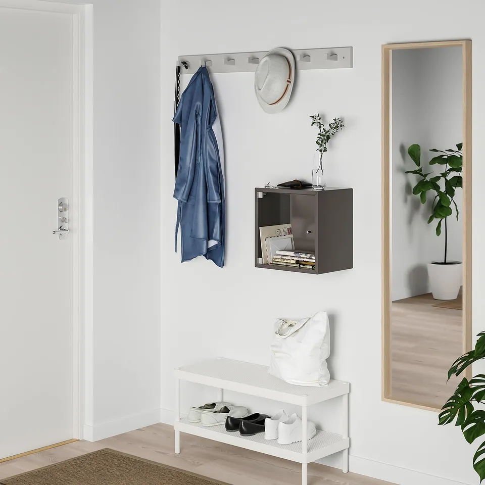 Modern entryway: coat rack, vase, bench, mirror, display case, plant.