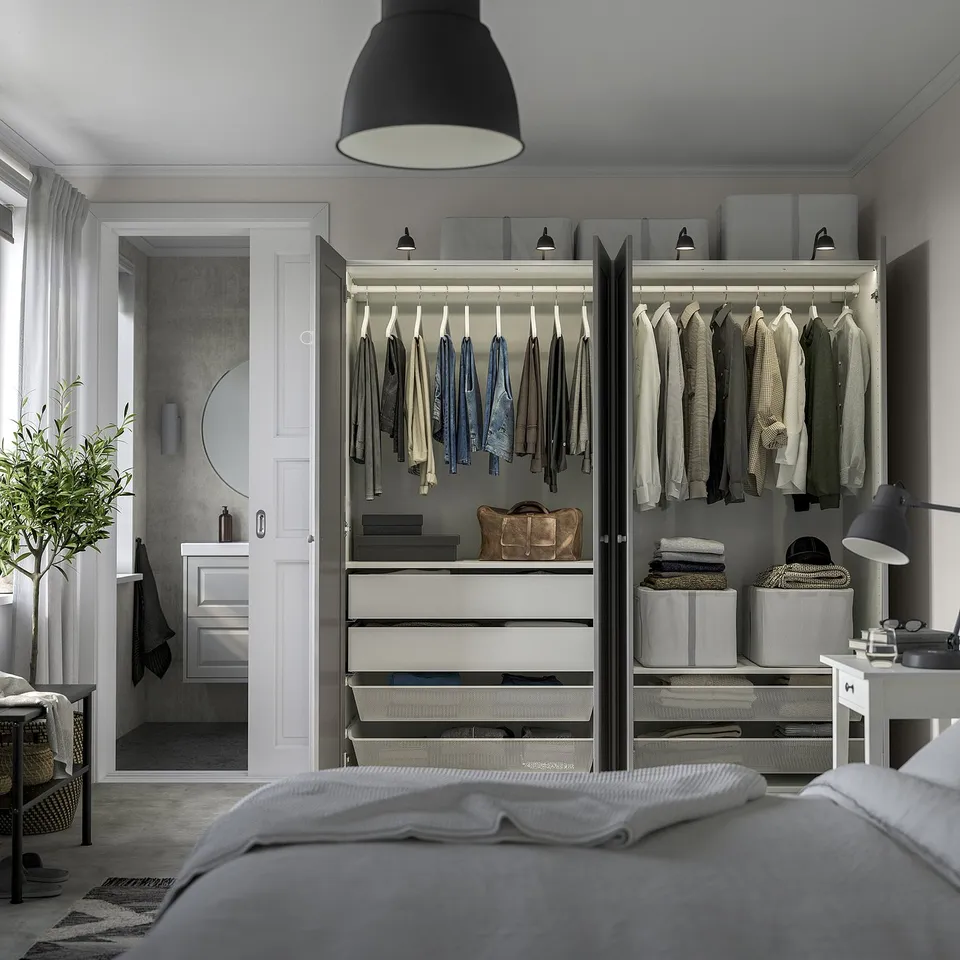 Modern bedroom with lit wardrobe, clothes, and plant. Clean layout with bed focused.