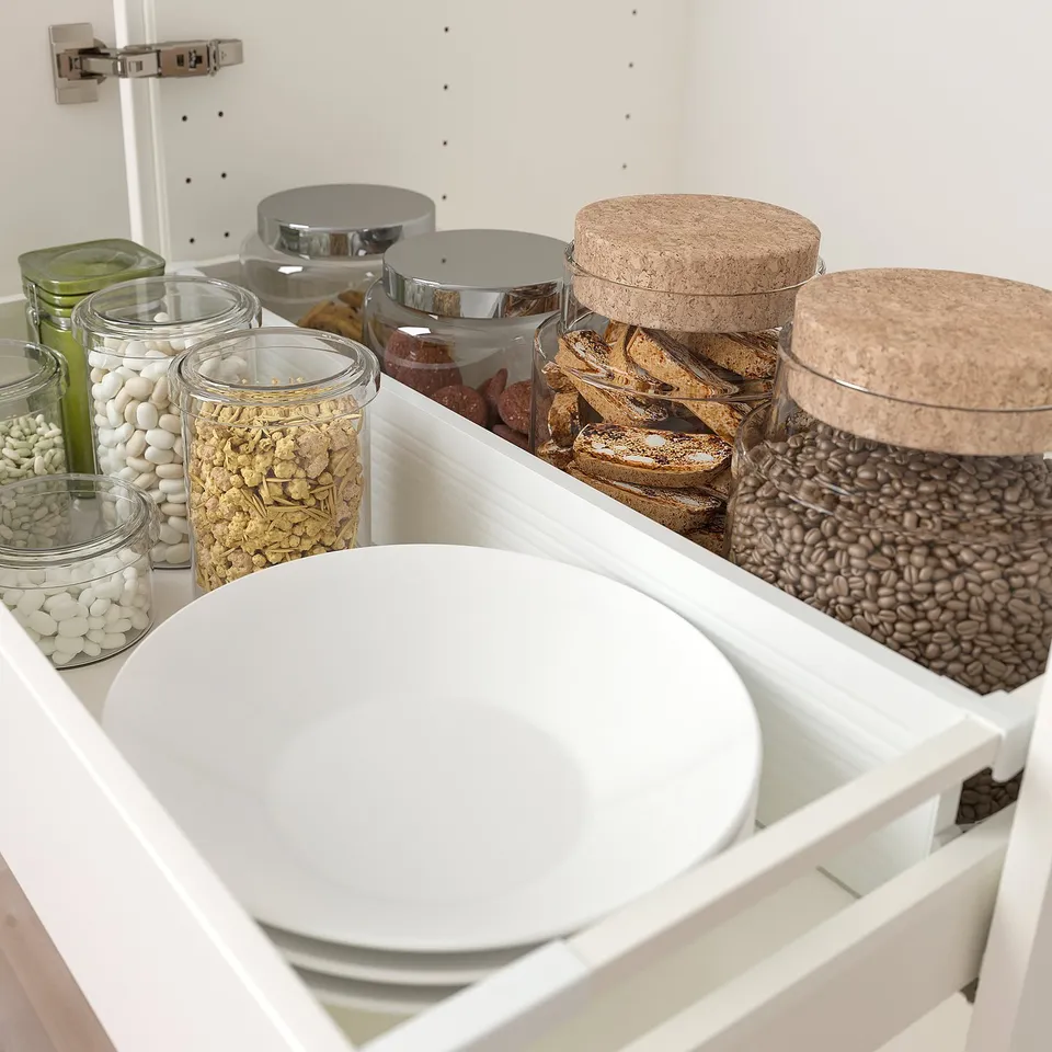 Open drawer organiser with glass jars and a white bowl, storing various food items.