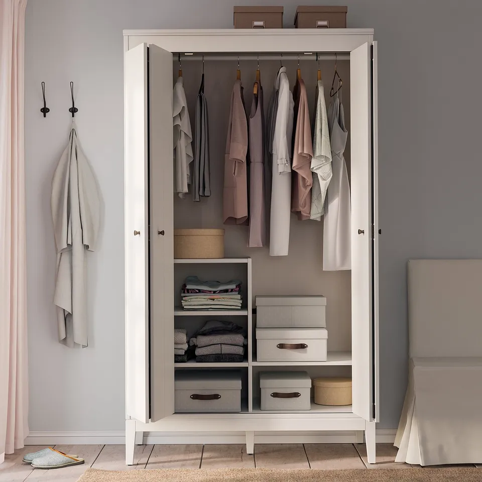 IDANÄS white wardrobe, open. Hangs pastel clothes, stacks folded clothes, boxes. Organised, modern design.