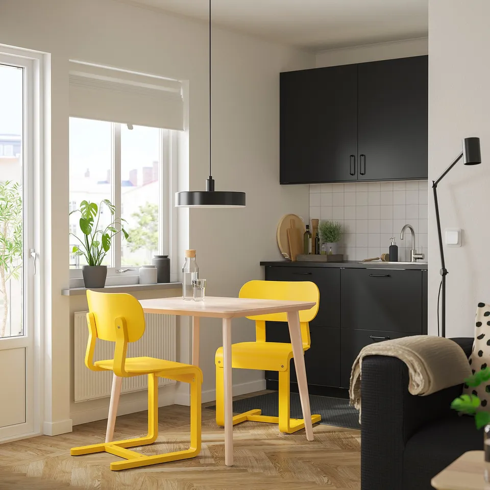Bright kitchen with small yellow LISABO chairs & table, modern design, black cabinets, large window, cosy decor.