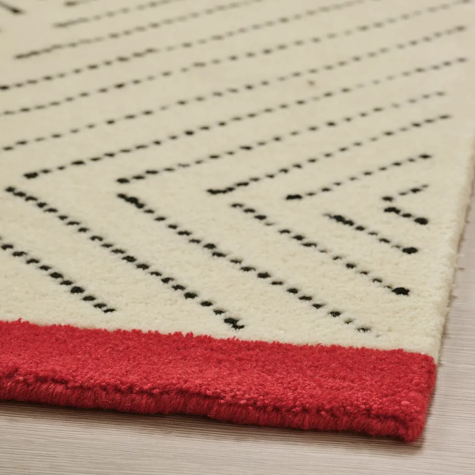 Modern rug with woven design, soft white wool, red edge, laid on wooden floor.