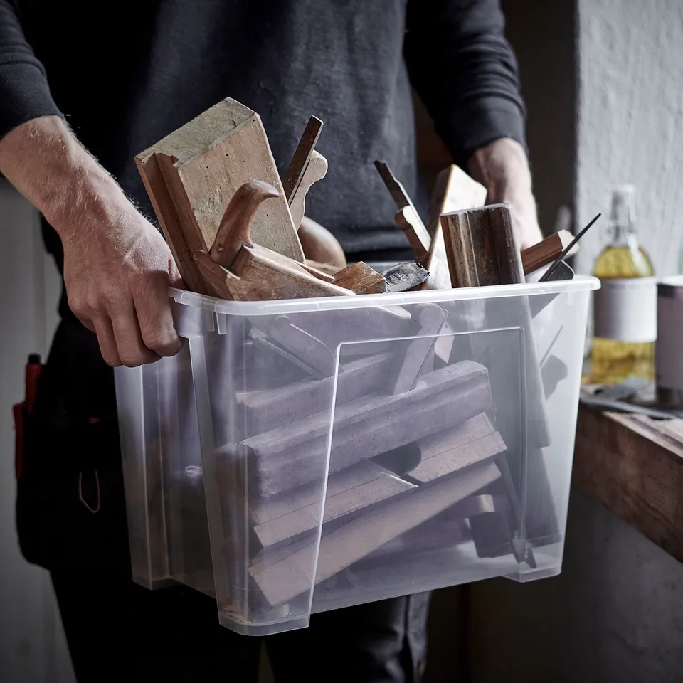 A person holds a clear plastic bin filled with wooden tools, ready for organising and storing.