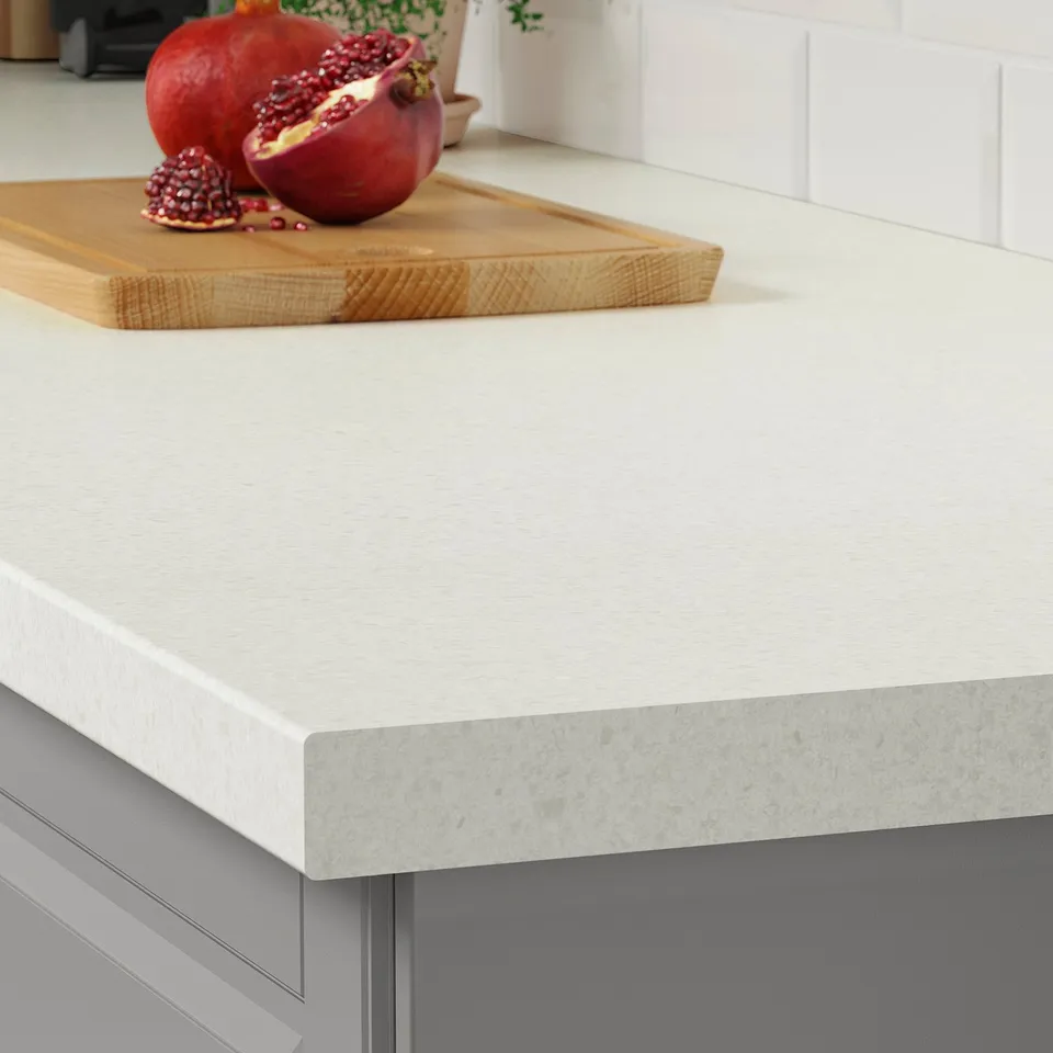 Modern kitchen countertop with stone pattern and rounded edges. Cutting board with pomegranates and fruit.