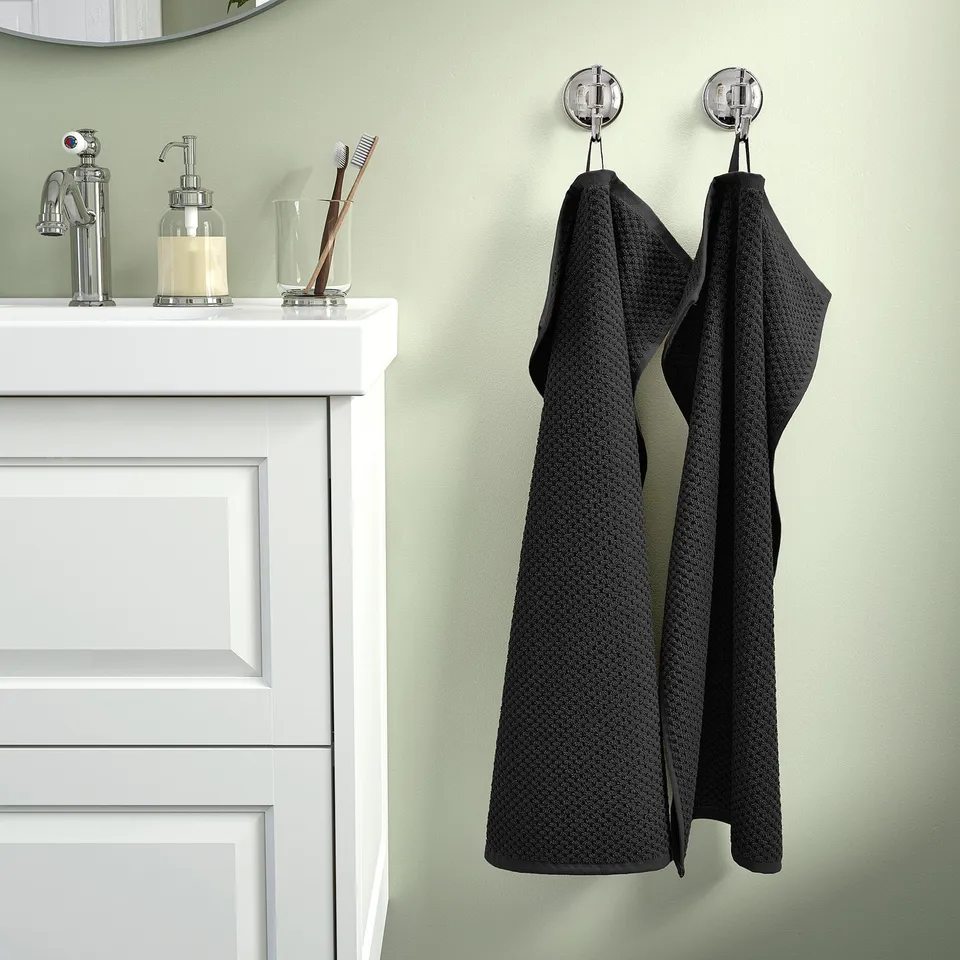 Black cotton towels on hooks beside white sink with toiletries.