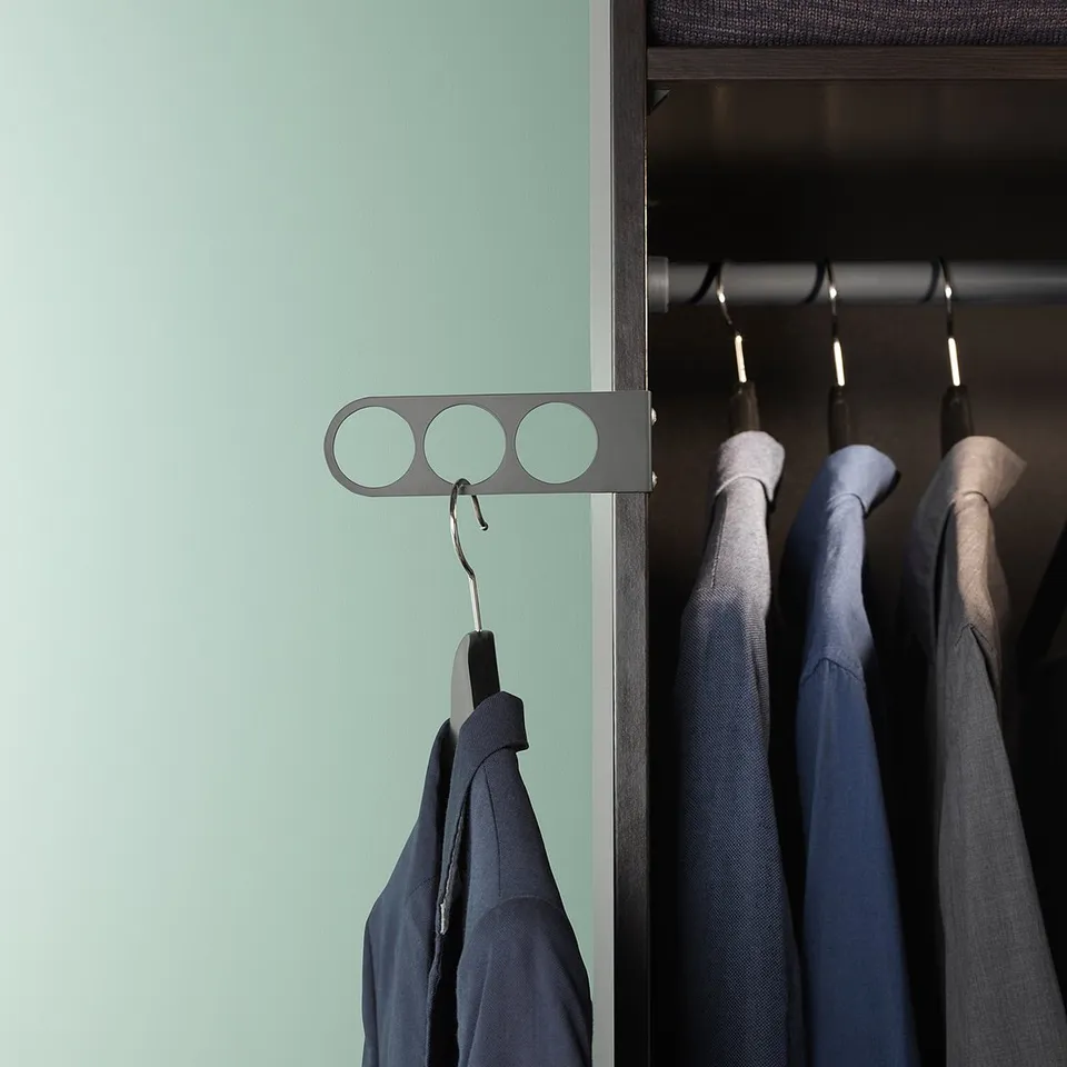 KOMPLEMENT grey valet hanger with three circular cutouts, hanging black coat, next to closet with dark clothes.
