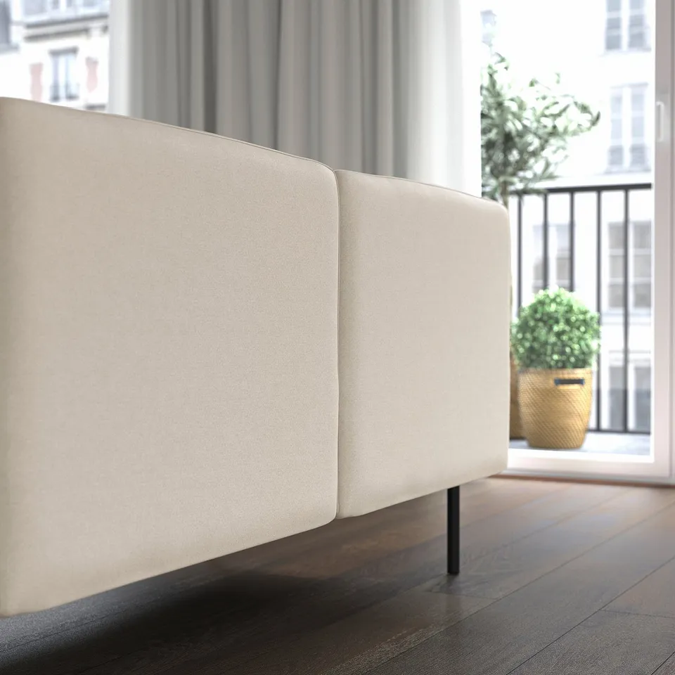 Modern sectional sofa in neutral fabric, positioned near a large window with potted plants outside. Ideal for versatile, supportive seating.