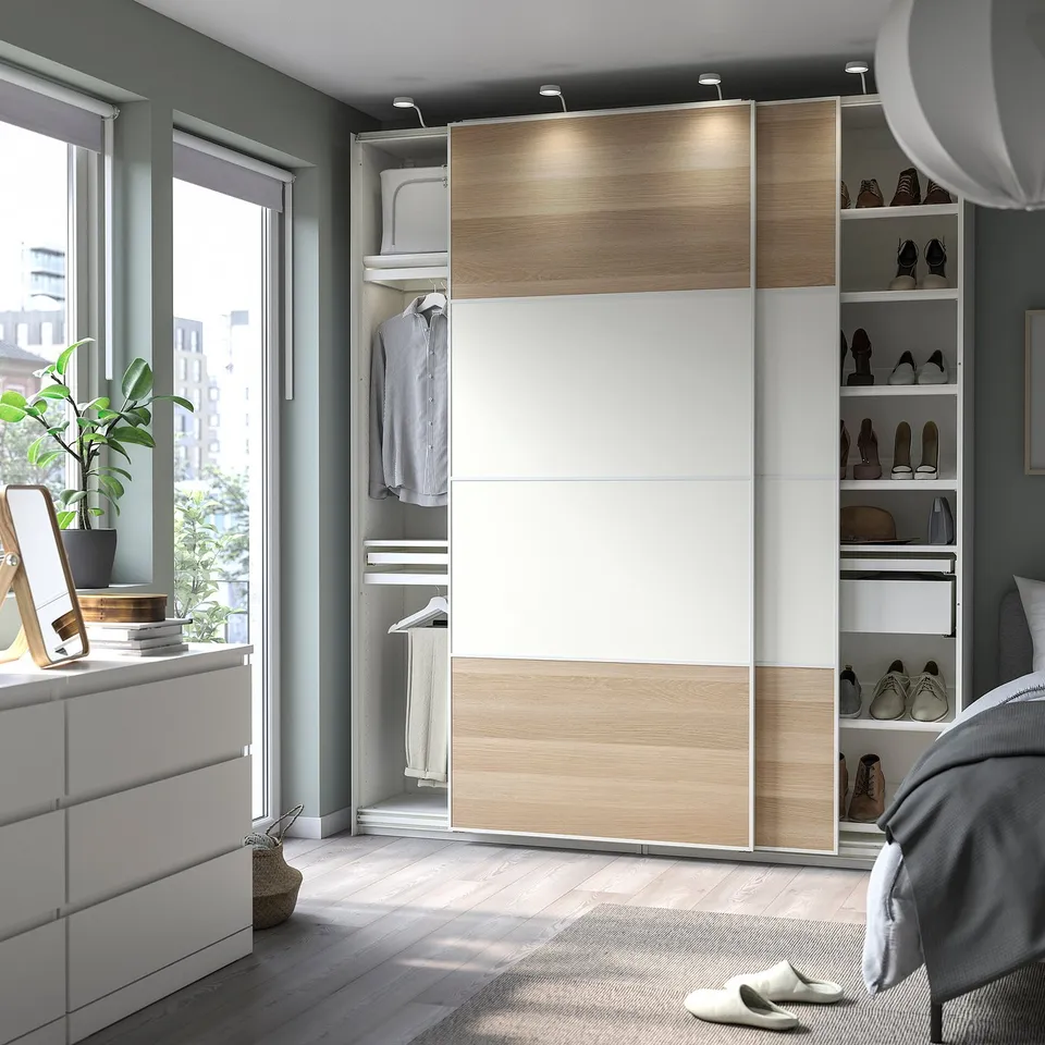 Modern white and wood wardrobe with sliding doors and shelves, a dresser, and a large mirror near a window.