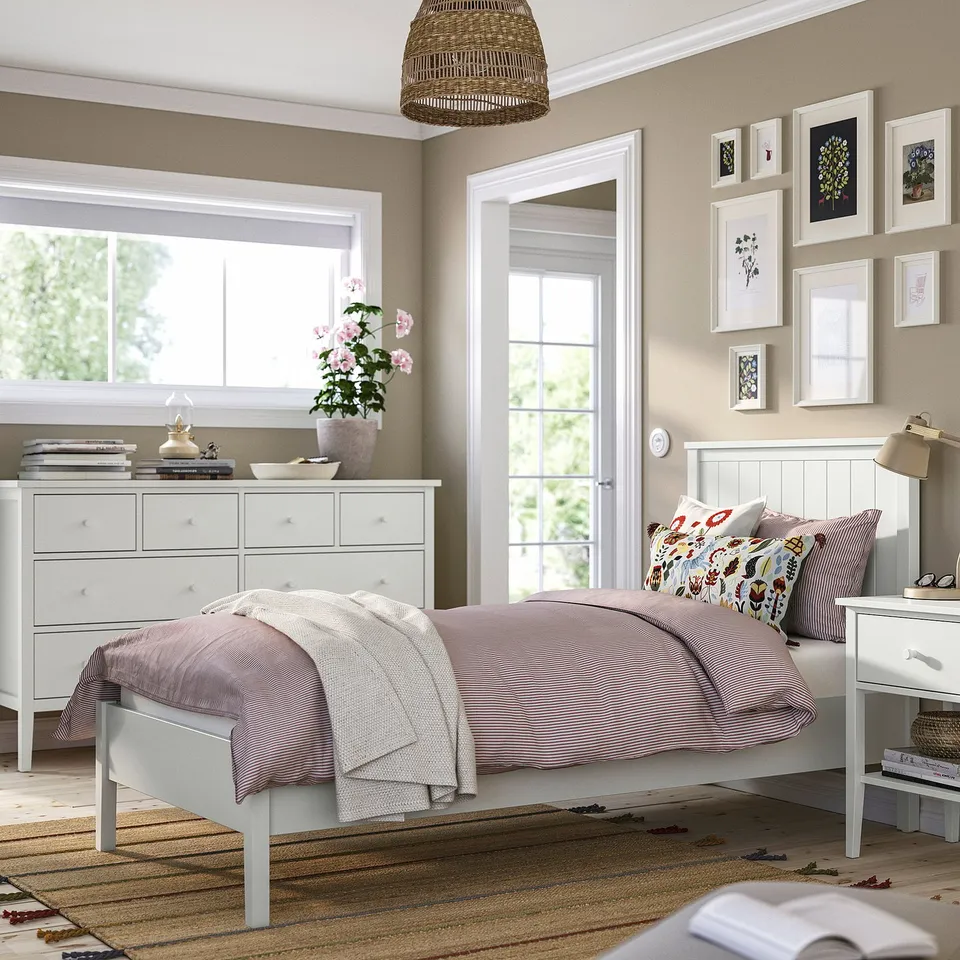 Bedroom with gullberg bed, striped linens, wooden headboard. Gullberg chest, bedside table, floral cushions. Window, mirror, artwork.