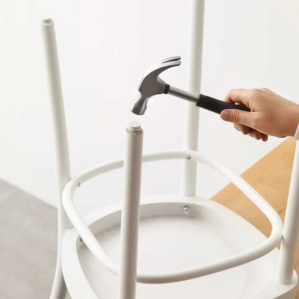 A hand uses a hammer to attach a floor protector to a white metal chair leg, preventing scratches and noise.
