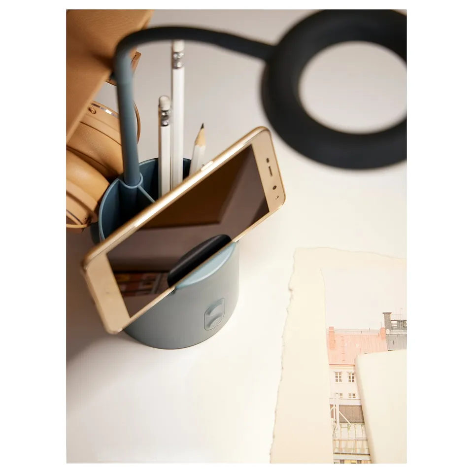 Organised workspace: golden phone, light blue pen holder with pens, black headphones, white paper.
