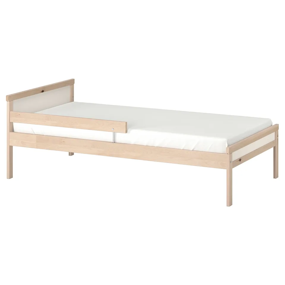 A light-colored wooden SNIGLAR bed with a white mattress. It is designed for children, with a guard rail for safety.
