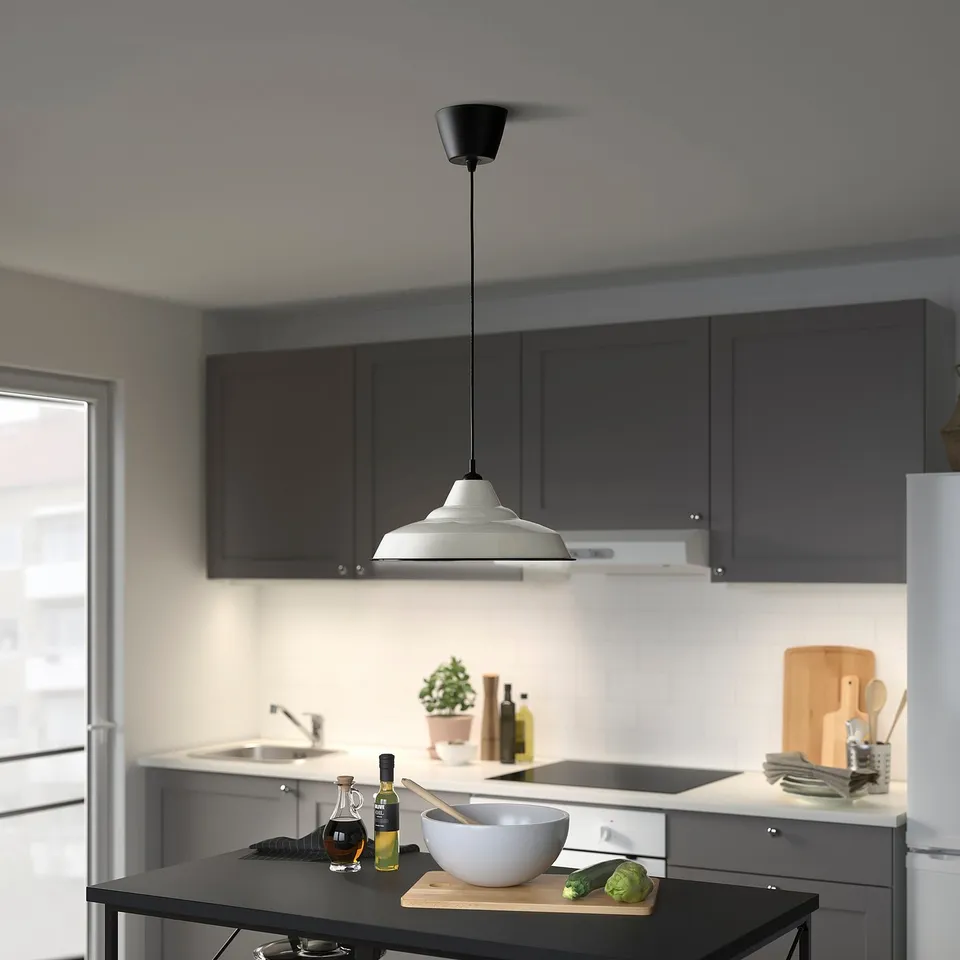 Modern kitchen with dark cabinets, white counters, TRETTIOEN lamp, veggies on cutting board.