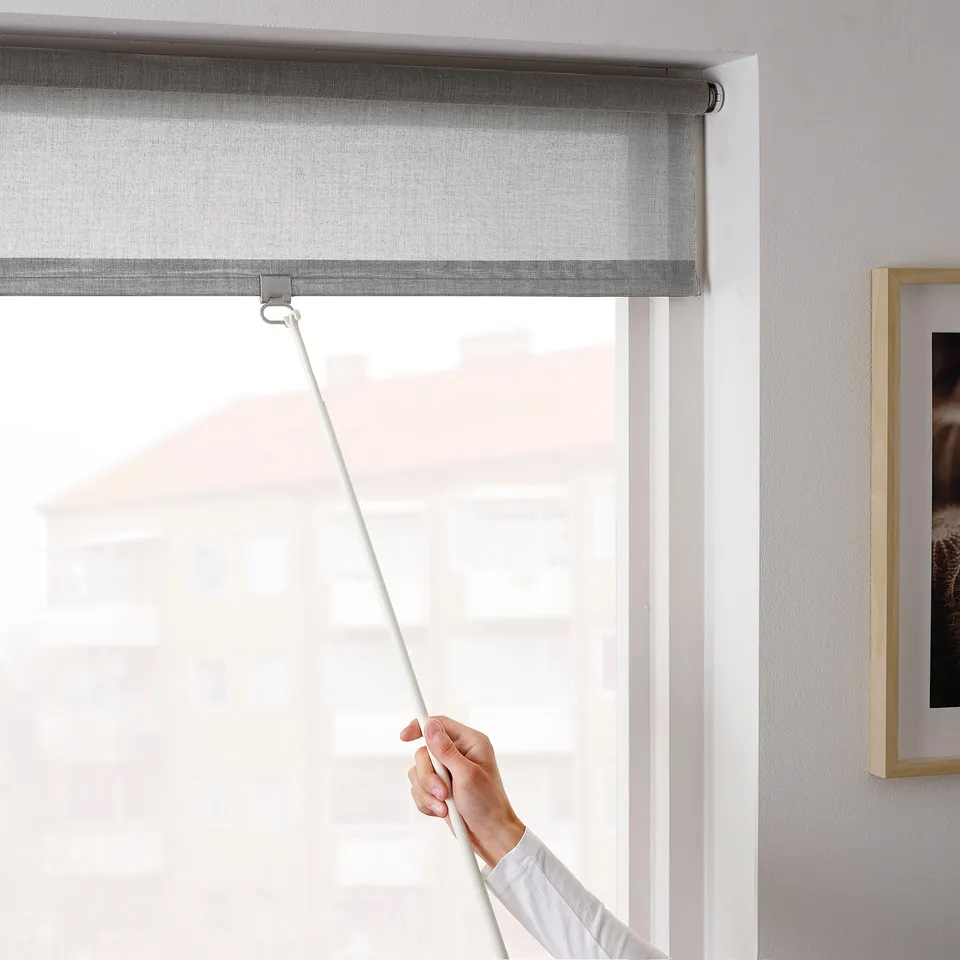 Hand pulls LÅNGDANS blind down, philtres light, ensures privacy, cordless for safety.