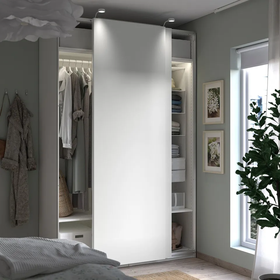 Modern grey PAX wardrobe with mirrored doors, clothes, and plant.