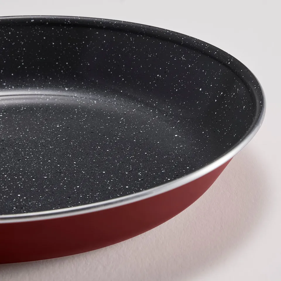 Close-up of a high-quality non-stick frying pan, sleek dark interior, vibrant red exterior, emphasising durability and heat efficiency.