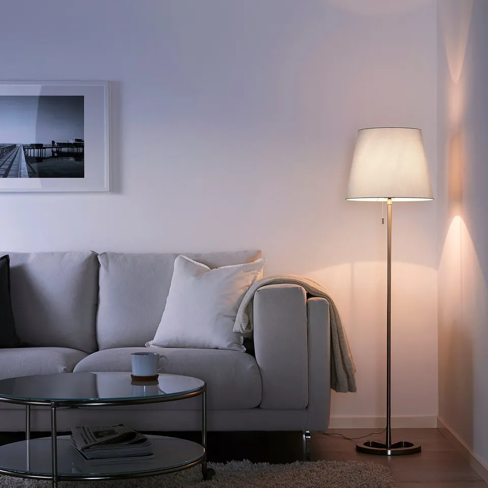 Living room with NYFORS lamp beside grey sofa, warm glow.