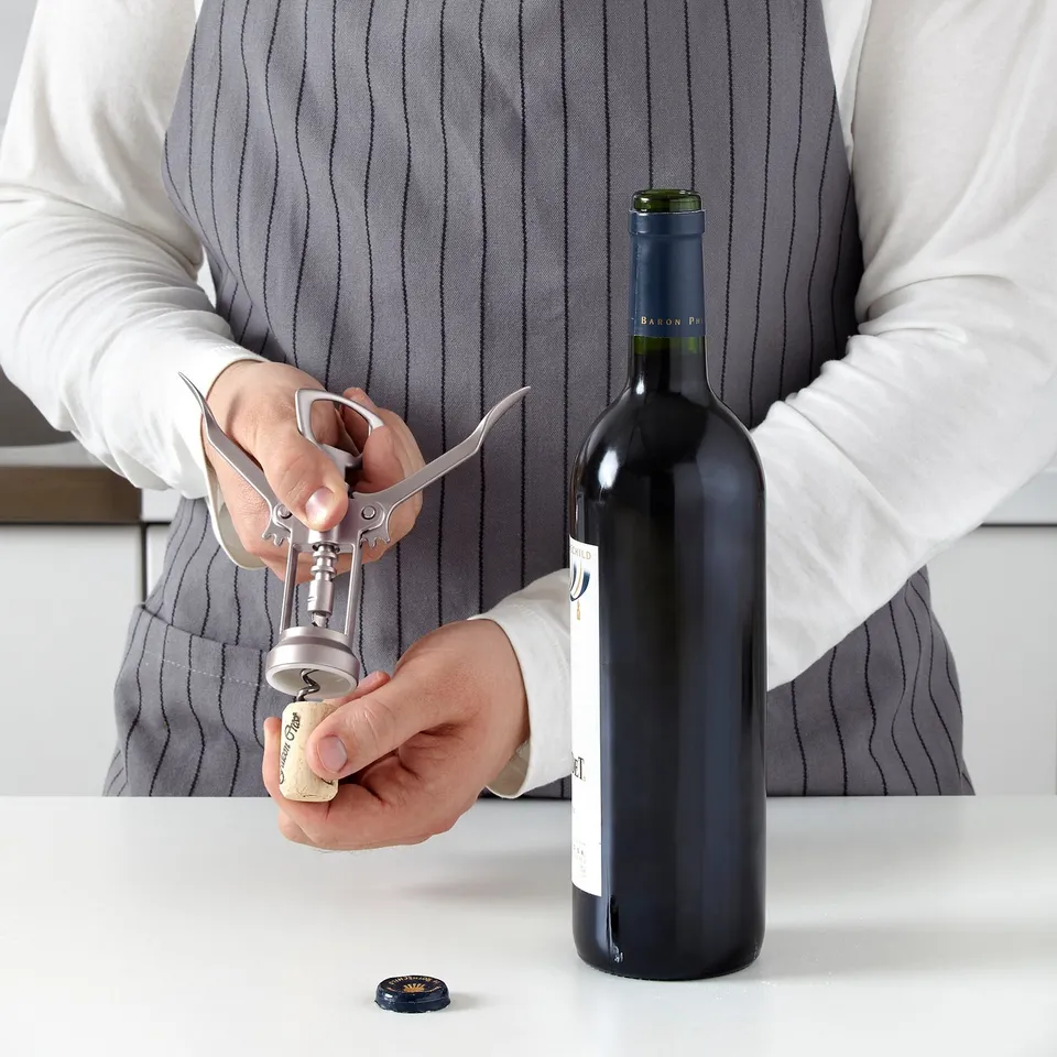 Person uses bottle opener to remove cork from wine bottle.