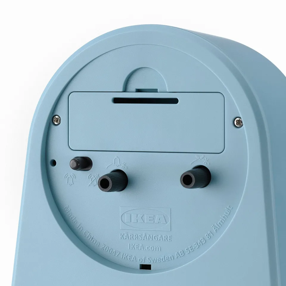 Back of light blue IKEA alarm clock with two knobs, tiny bell icon, and labels.