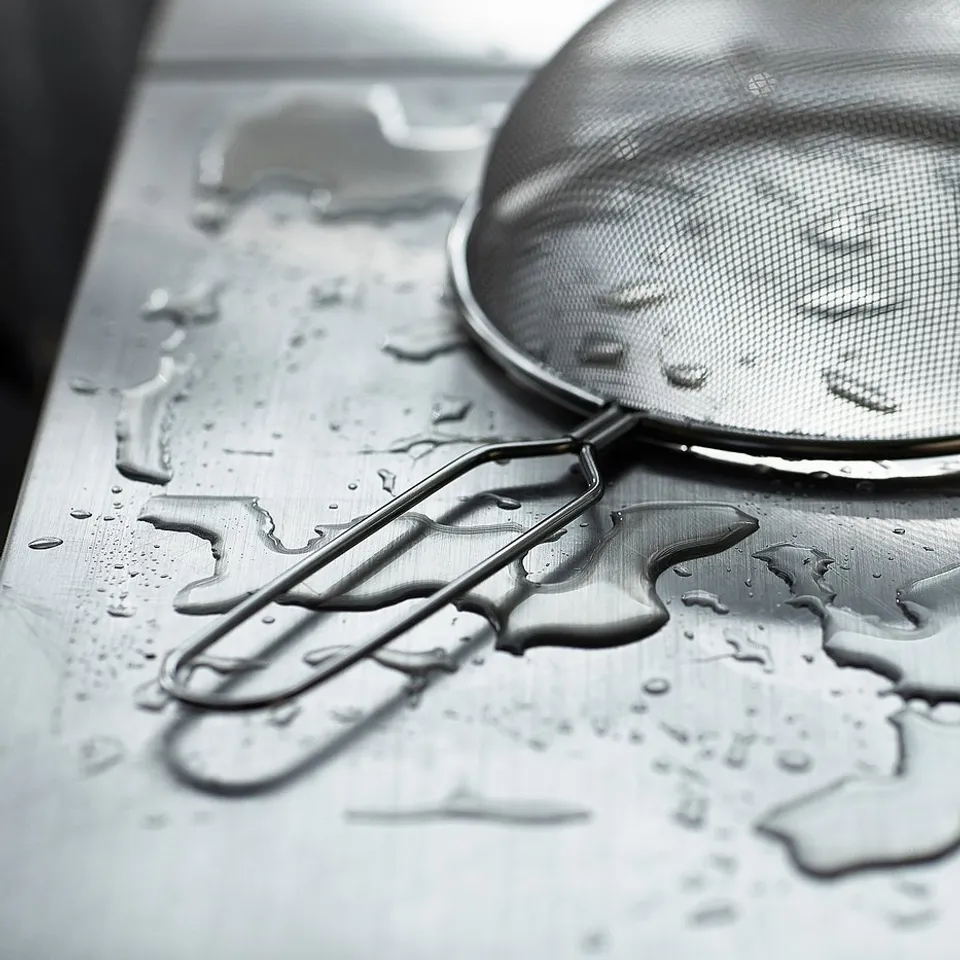 Black and white a stainless steel strainer with water droplets on a table.