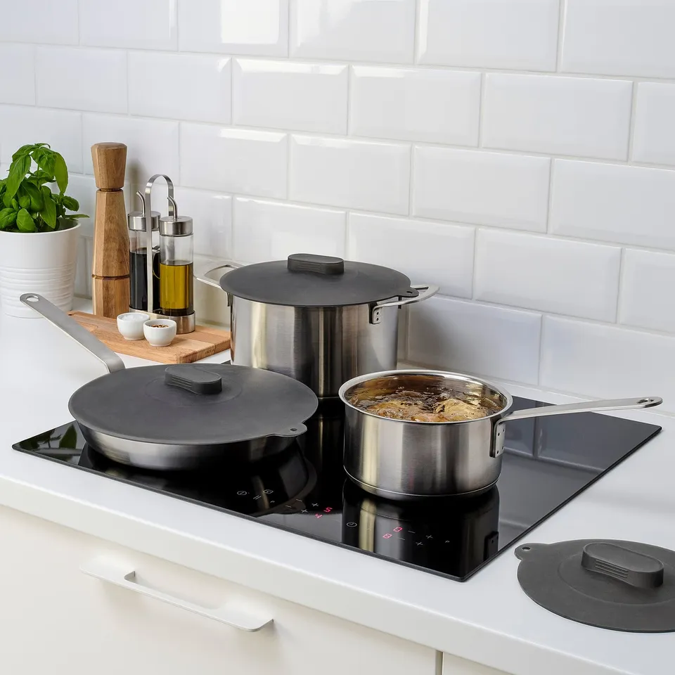 Modern kitchen with stainless steel pots on sleek electric stove, using silicone lids for even heat.