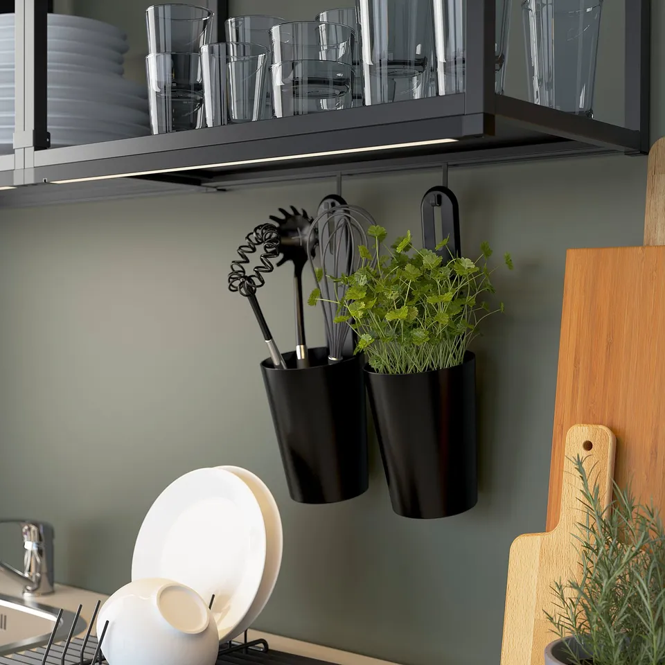 Kitchen storage with hanging pots, utensils, and herbs. Glassware in cabinet above. Wooden chopping board on the right.